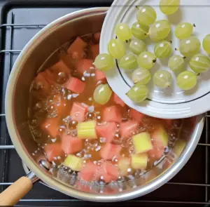 Cooking rhubarb with sugar, maple syrup, and water in a saucepan before adding gooseberries.
