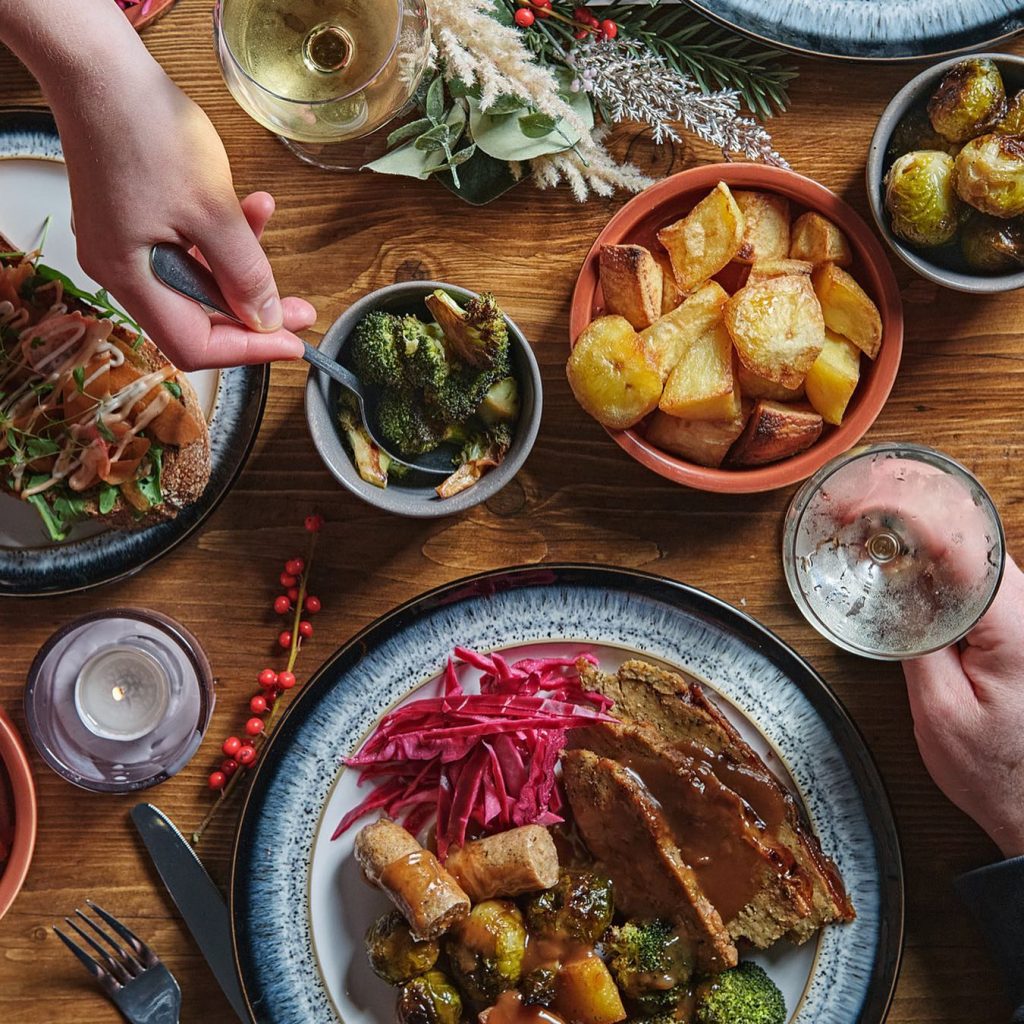 A vegan Christmas table with seitan roast, roast tatties, kilties, brussel sprouts, steamed broccoli, glazed carrots and parnsips, pickled red cabbage and gravy